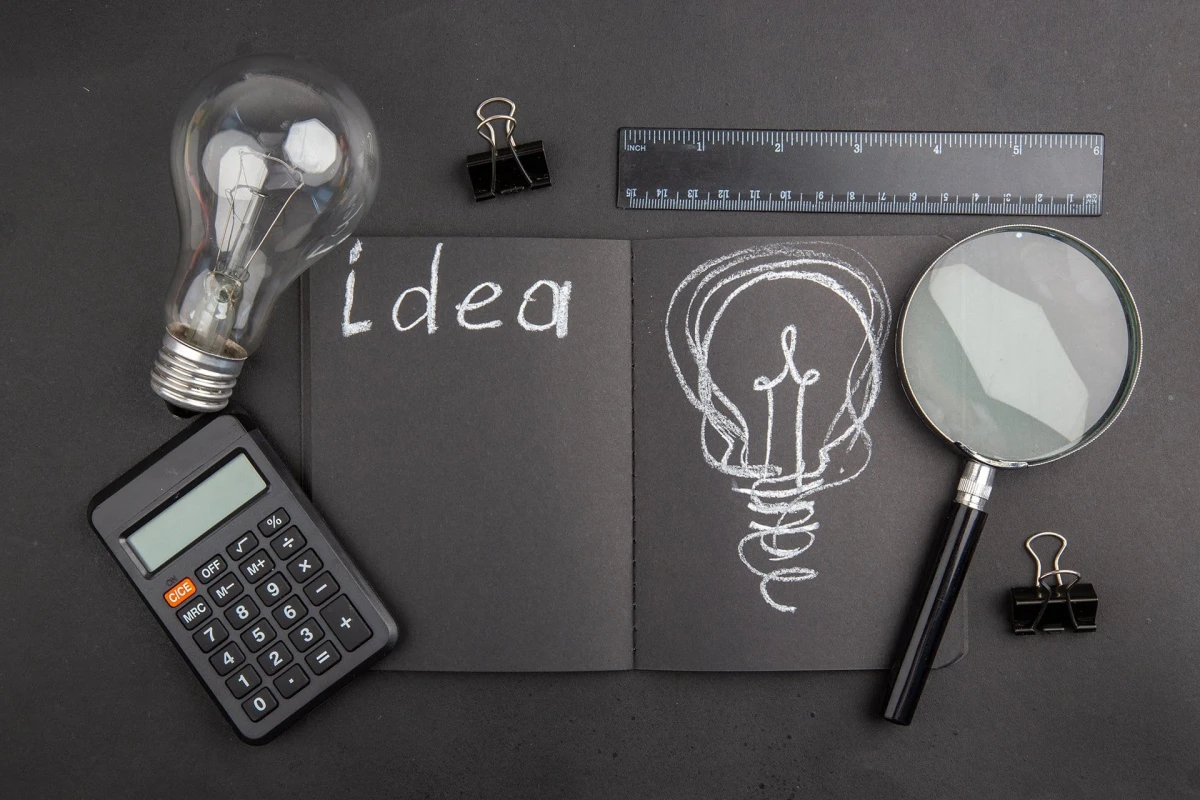 top view idea written on black notepad light bulb binder clips l